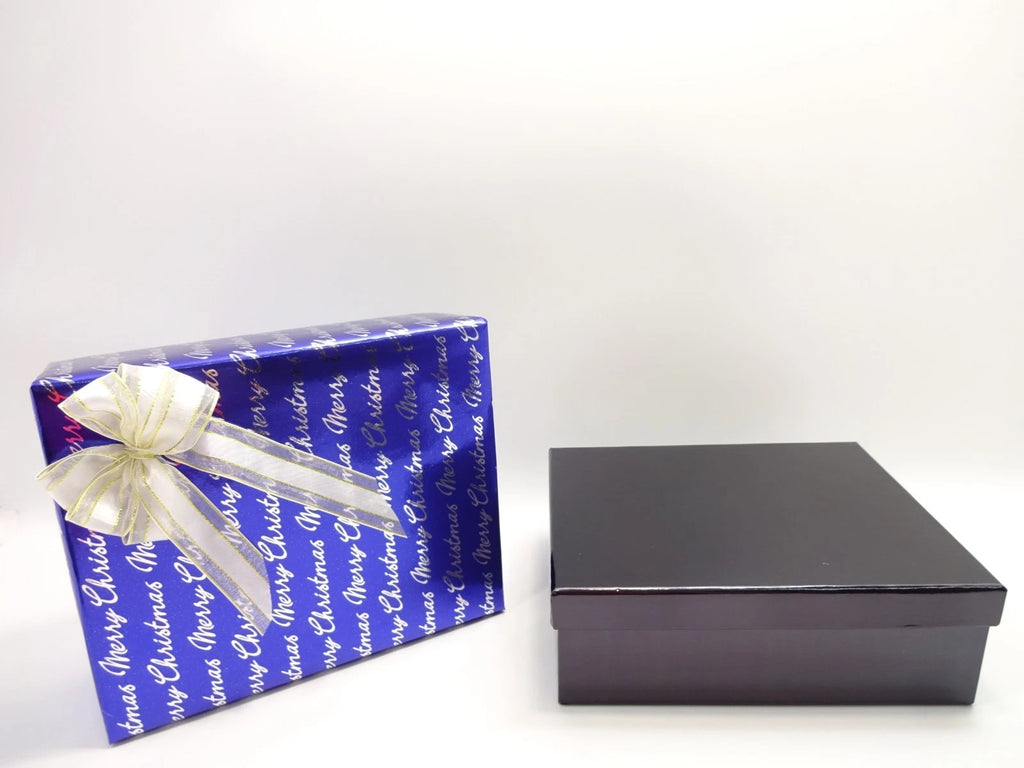 Close-up of blue Merry Christmas gift wrap featuring gold accents and white ribbon bow for men’s festive gift set.
