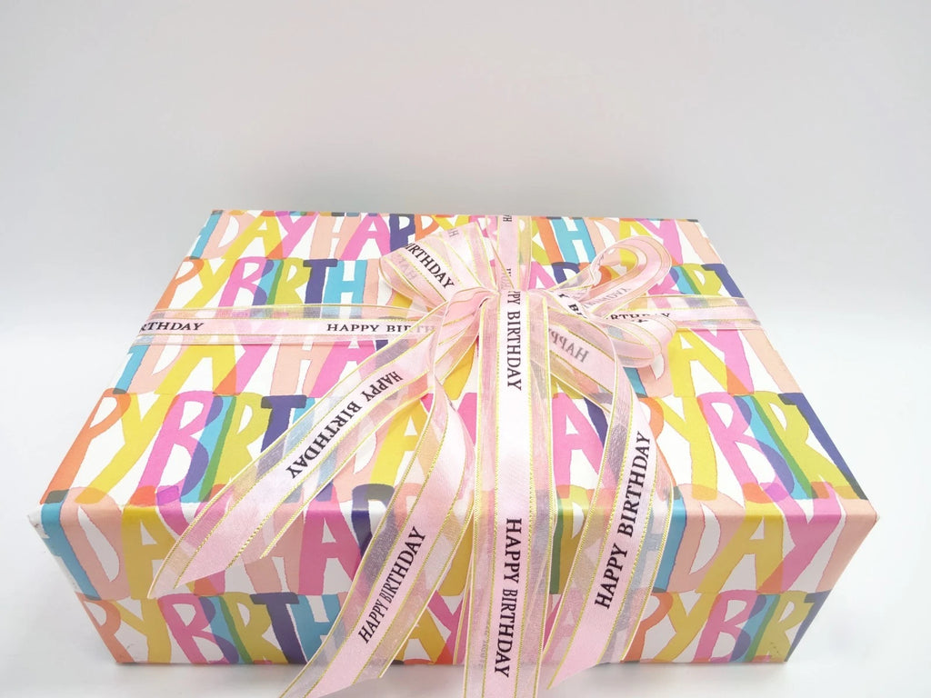 Gift box with colorful 'Happy Birthday' wrapping paper and pink ribbon on a white background