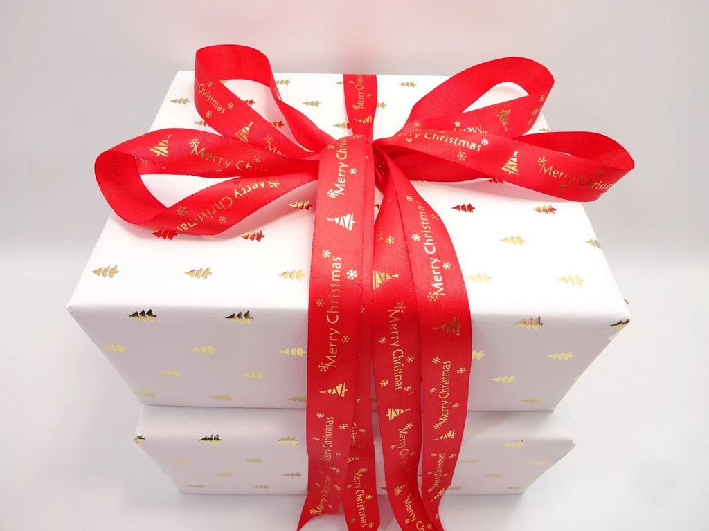 White Christmas box decorated with gold tree prints and red “Merry Christmas” ribbon bow for festive presentation.