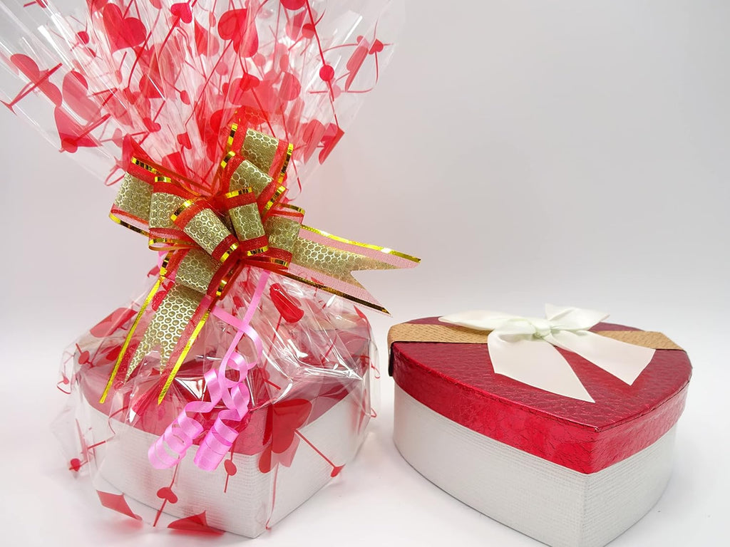 Wrapped red heart-shaped gift box with transparent heart-patterned cellophane and gold ribbon bow