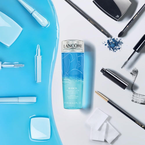 Lancôme Bi-Facil Eye Makeup Remover 125ml bottle flatlay with makeup essentials and spilled cleansing liquid