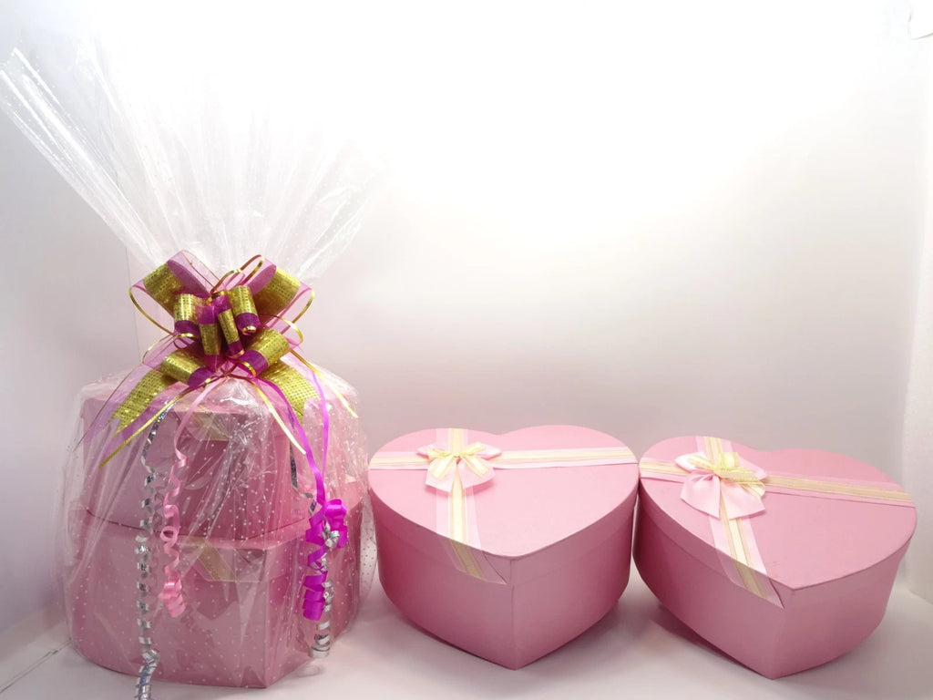 Two-tier pink heart-shaped gift boxes wrapped in cellophane with gold and pink bow and ribbon