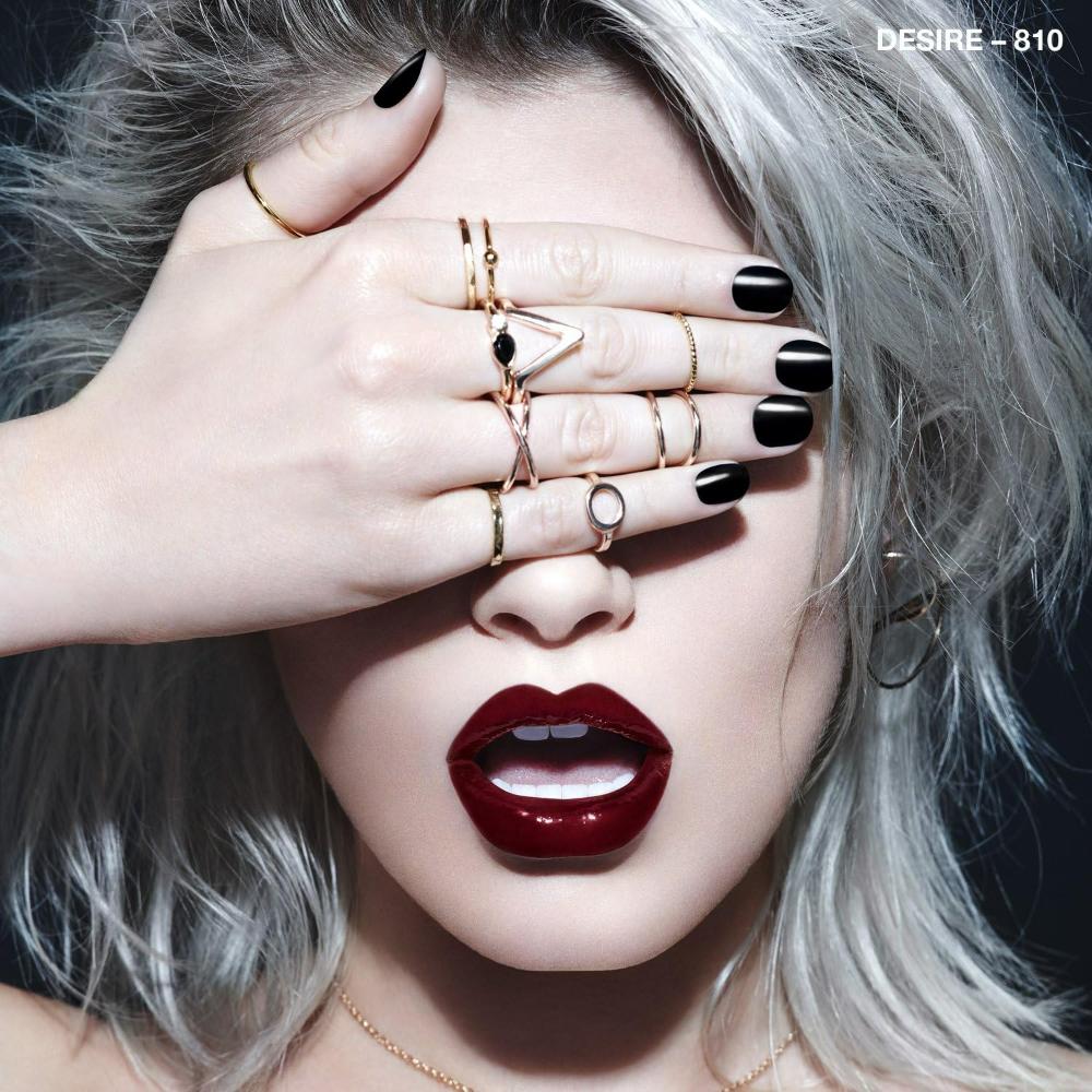 Model with platinum hair and bold accessories wearing Rimmel Rita Ora 810 Desire on lips for a striking look