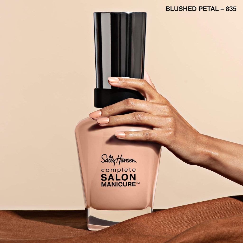 Hand model holding Sally Hansen 835 Blushed Petal nail polish, showcasing glossy nude pink manicure