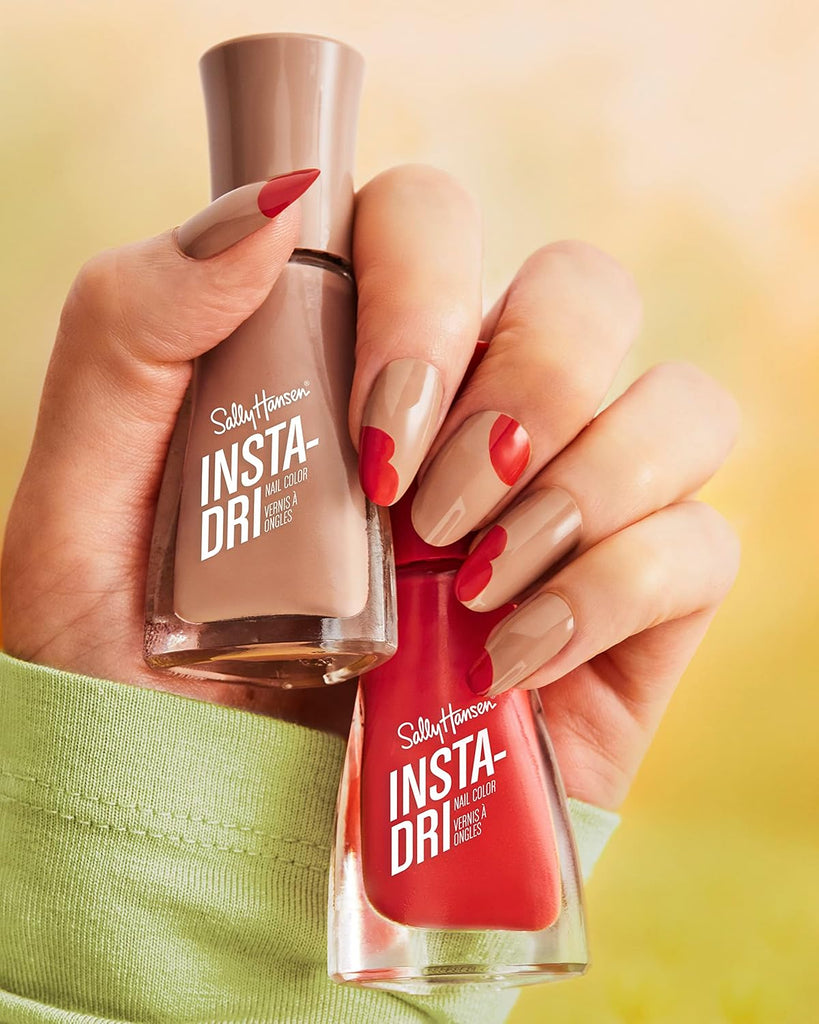 Hand holding Sally Hansen Insta-Dri nail polishes in nude beige and bright red, creative nail art design with heart tips and accent colors