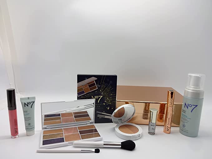 Boots No7 makeup and skincare collection including a palette, foundation, and brushes displayed next to a gold gift box.